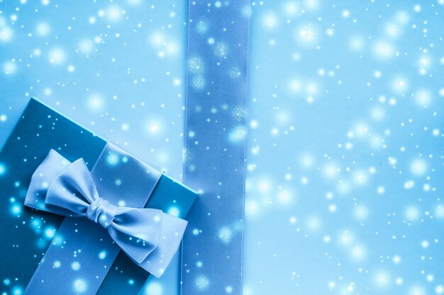 Winter holiday gifts and glowing snow on frozen blue background Christmas presents surprise