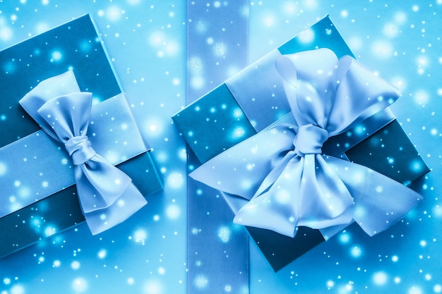 Winter holiday gifts and glowing snow on frozen blue background Christmas presents surprise