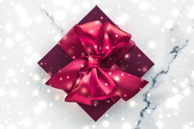 Winter holiday gifts with cherry silk bow and glowing snow on frozen marble background Christmas presents surprise