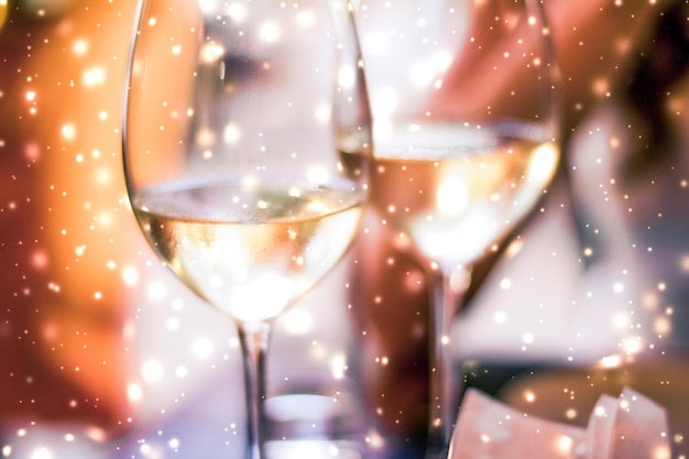 Winter holiday glasses of white wine and glowing snow on background Christmas time romance