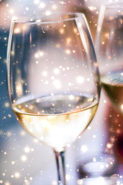 Winter holiday glasses of white wine and glowing snow on background Christmas time romance