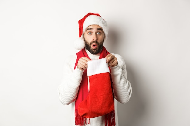 Winter holidays and celebration concept. Surprised bearded man looking inside Christmas sock, receiving New Year gift, standing over white background