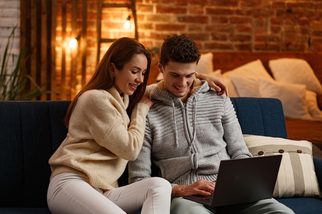 Winter holidays, Christmas celebrations, New Year concept. Portrait of beautiful smiling couple watching Christmas movie at home. Beautiful young couple at home enjoying spending time together.