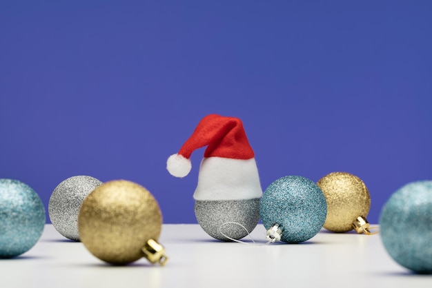 Winter holidays, Christmas sparkling balls, one in a Santa hat. Blue background, light surface,