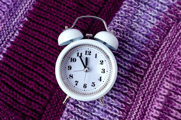 Winter is the time for needlework: white clock on a lilac knitted product, close-up, top view