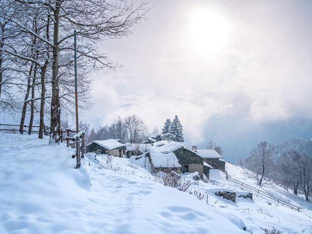 Winter in the italian Alps Beautiful view of idyllic village in snowy forest and snowcapped mountain peaks Piedmont Italy