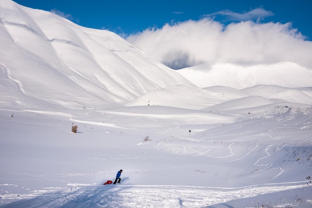 Winter landscape child with sledge in valley covered with snow