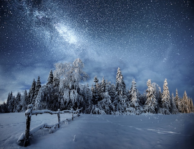 Winter landscape. Mountain village in the Ukrainian Carpathians. Vibrant night sky with stars and nebula and galaxy. Deep sky astrophoto.