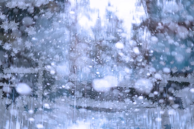 Winter landscape through a frozen window. Blurred snow background. Trees and plants covered with snow.