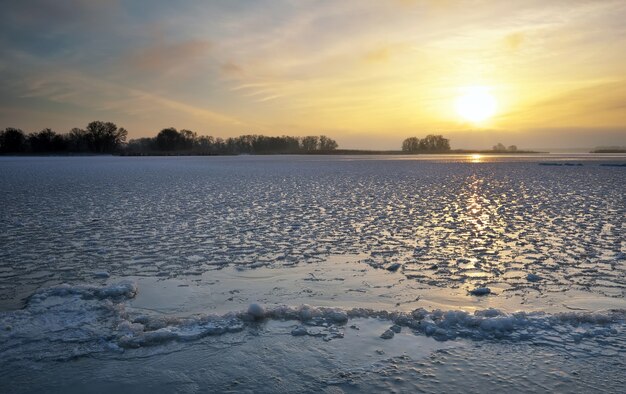 Winter landscape with lake and sunset fiery sky. Composition of nature.