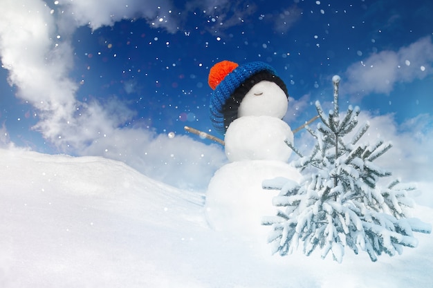 Winter landscape with a snowman and a snowcovered Christmas tree on a blue sky background