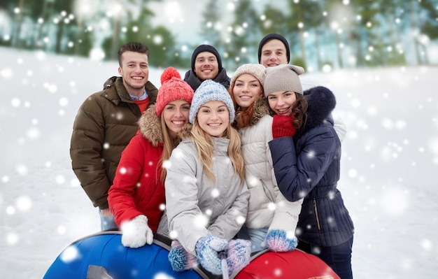 winter, leisure, friendship, technology and people concept - group of smiling young men and women with snow tubes taking picture with smartphone selfie stick outdoors