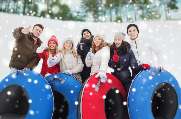 winter, leisure, sport, friendship and people concept - group of smiling friends with snow tubes showing thumbs up outdoors