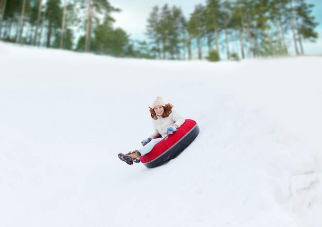 winter, leisure, sport, and people concept - happy teenage girl or woman sliding down on snow tube