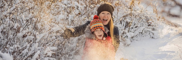 Winter mother and son throwing snowball at camera smiling happy having fun outdoors on snowing