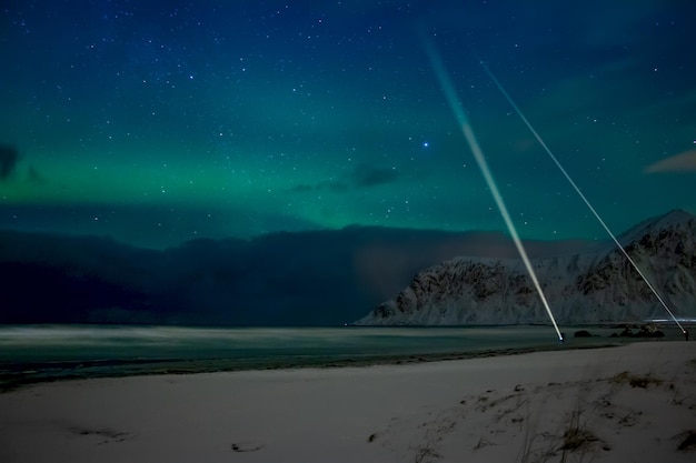 Winter Norway. Night beach between the mountains in Lofoten. Light northern lights and people with flashlights