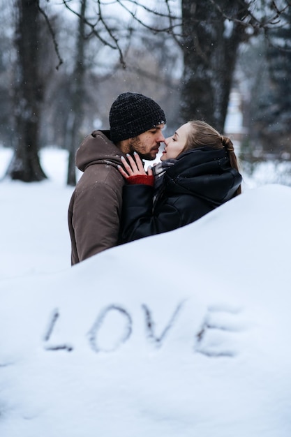 Winter outdoors portrait of young couple in love and word love on snow valentines day outdoors