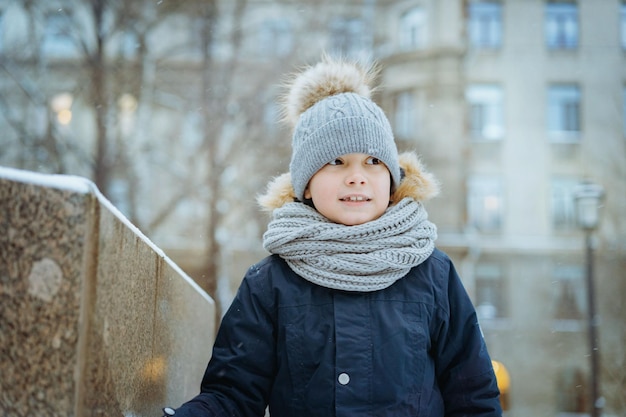 Winter portrait of cute caucasian 7 years old boy in knit hat with pompom in city