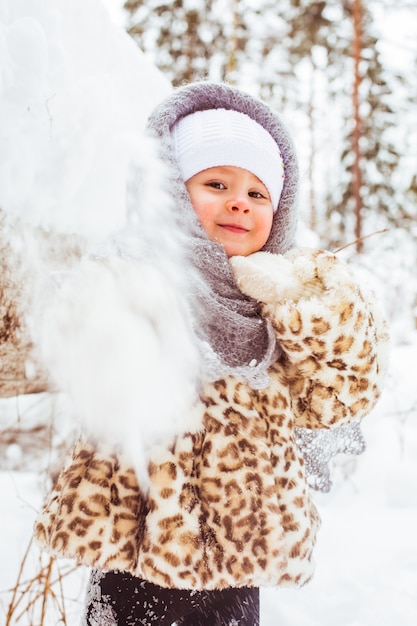 Winter portrait of cute smiling child girl on the walk in sunny snowy forest