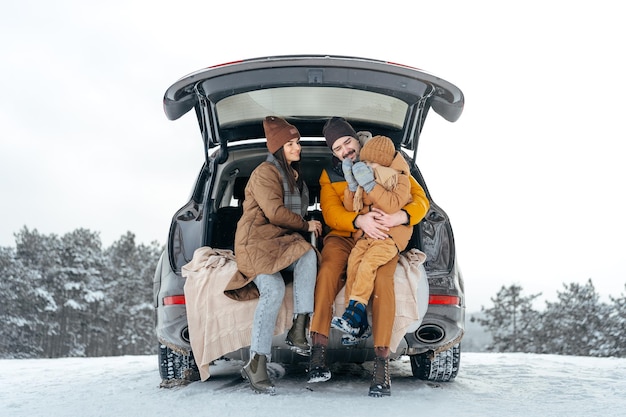 Winter portrait of a family sit on car trunk enjoy their vacation in forest