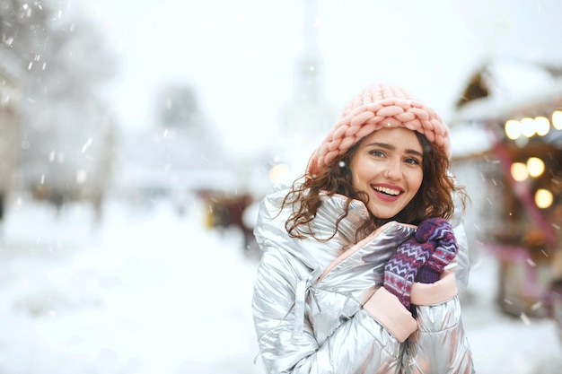 Winter portrait of a young woman walking at the Christmas fair during the snowfall. Empty space