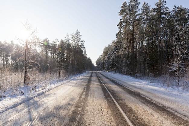 Winter time on a narrow road in the forest, the road is covered with snow after snowfall, frosty weather on a slippery and dangerous road for transport