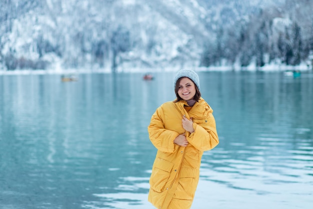 Winter travel across Europe. portrait of a beautiful young woman in a yellow jacket on the shore of an alpine lake in winter. view of the alpine lake with snow.