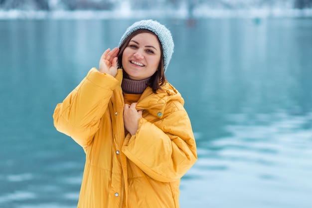 Winter travel across Europe. portrait of a beautiful young woman in a yellow jacket on the shore of an alpine lake in winter. view of the alpine lake with snow.