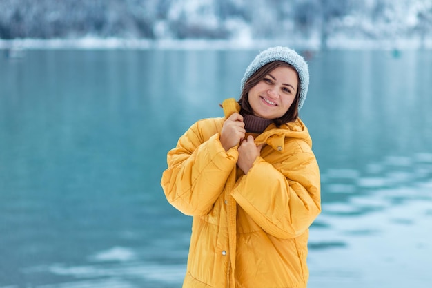 Winter travel across Europe. portrait of a beautiful young woman in a yellow jacket on the shore of an alpine lake in winter. view of the alpine lake with snow.