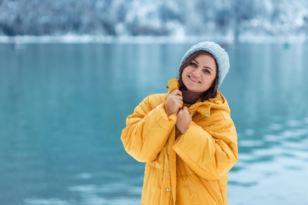 Winter travel across Europe. portrait of a beautiful young woman in a yellow jacket on the shore of an alpine lake in winter. view of the alpine lake with snow.