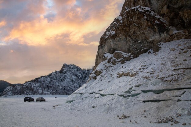 Winter travel by car Winter landscape mountains and rocks covered with forest on the bank of a frozen river against the sunset sky