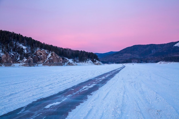 Winter travel An icy road along a frozen river bed mountains on the horizon a pink sunset sky Winter landscape beauty of nature