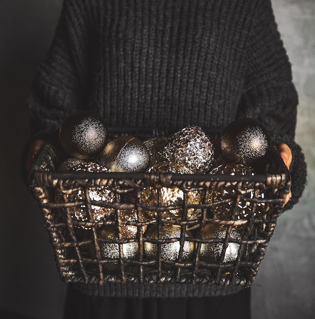 Wire basket full of Christmas or New Year tree golden vintage decoration toys in hands of lady in a gray warm sweater, selective focus, square crop