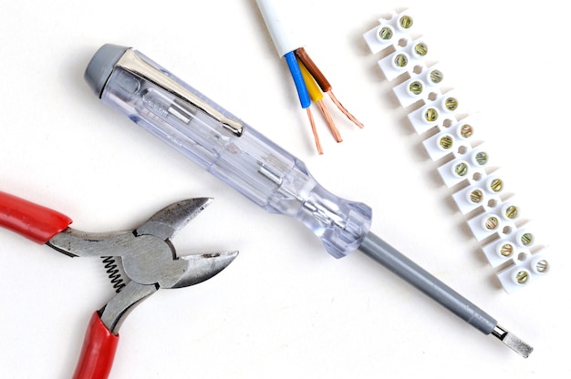 Wire cutters, stripped wire, tester screwdriver and terminal block. on a white background, top view.