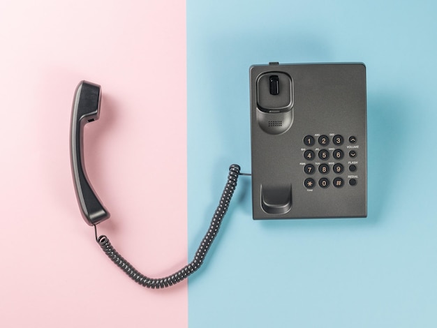 A wired phone with buttons and a handset lying next to it on a blue and pink background Flat lay