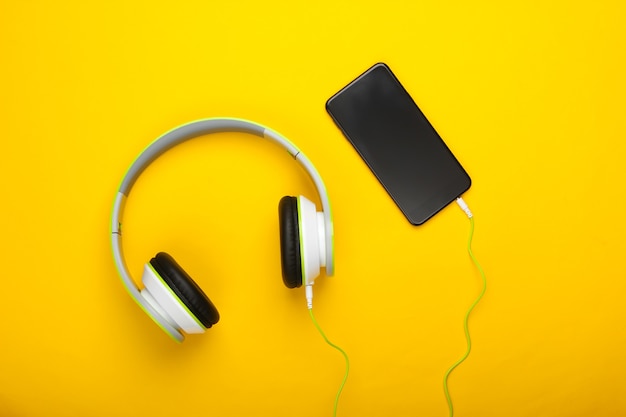 Wired stereo headphones with smartphone on yellow surface. Millennial stuff