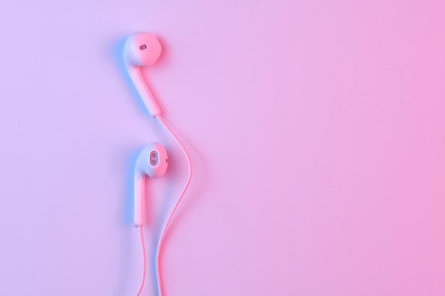 Wired white earphones isolated on white background closeup in pink neon light