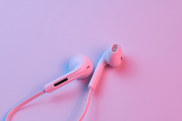 Wired white earphones isolated on white background closeup in pink neon light