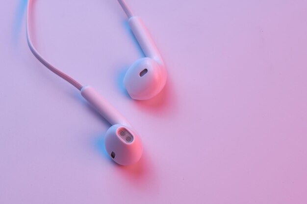 Wired white earphones isolated on white background closeup in pink neon light