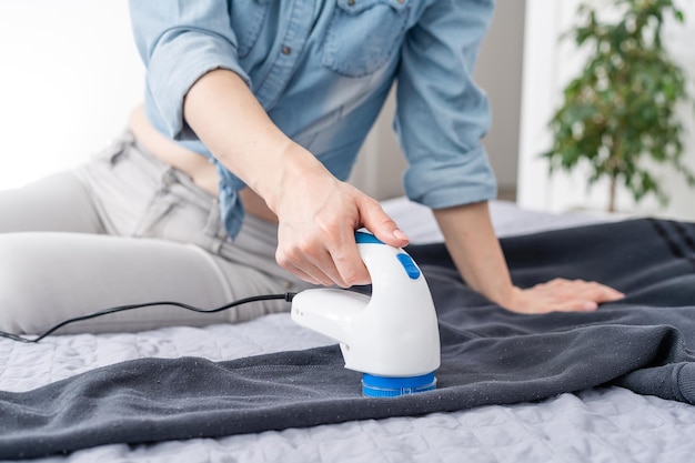 Wireless device for cleaning knitted fabrics from lint. The woman is removing the lint from the sweater.