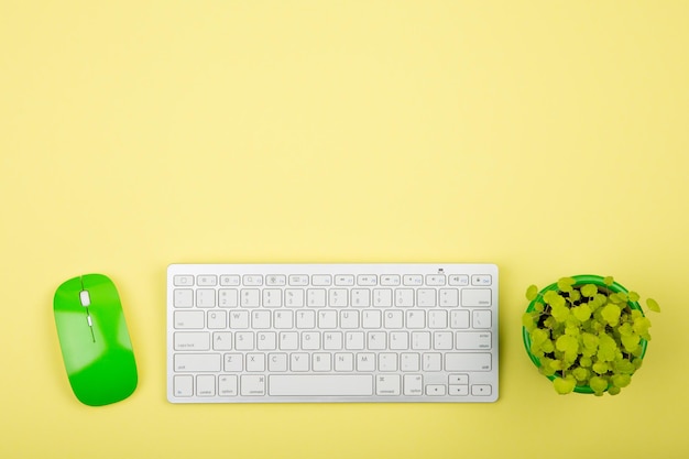 Wireless slim white keyboard and green mouse on yellow background