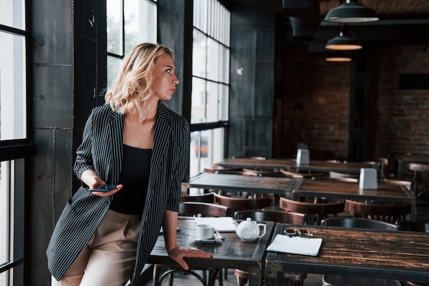 Wireless technologies. Businesswoman with curly blonde hair indoors in cafe at daytime.