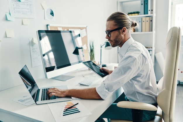 Wireless technology. Good looking young man in shirt using digital tablet while sitting in the office