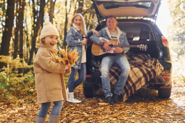 With acoustic guitar Happy family is in the park at autumn time together