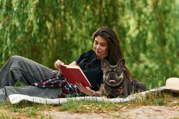 With book lying down Young pretty woman is with her dog in the park