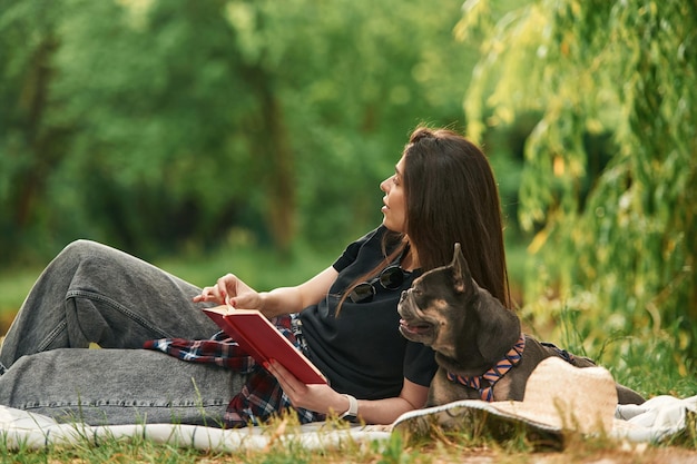 With book lying down Young pretty woman is with her dog in the park