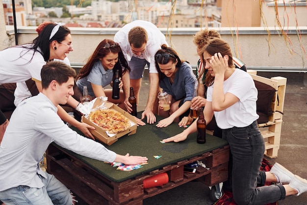 Photo with delicious pizza group of young people in casual clothes have a party at rooftop together at daytime