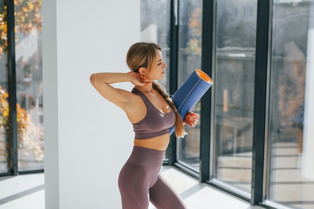 With fitness mat Woman in sportive clothes doing yoga indoors