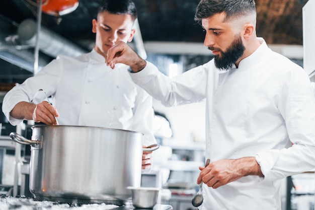 With help from other employee Chef in white uniform cooking food at kitchen Busy day at work