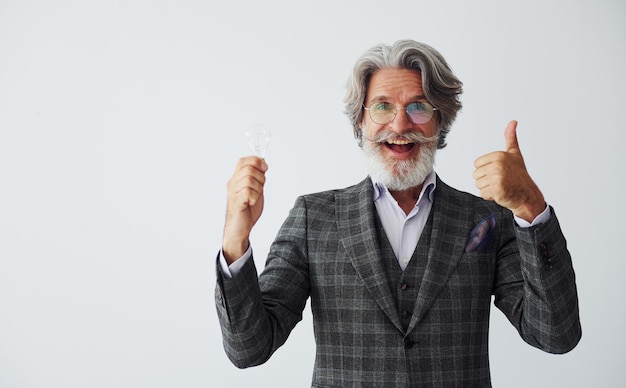 With light bulb in hands Senior stylish modern man with grey hair and beard indoors